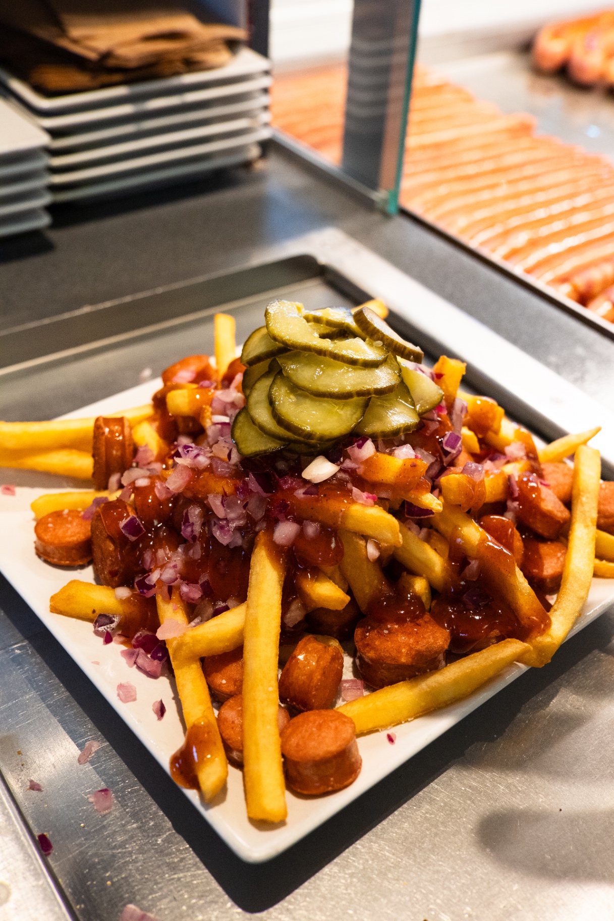 Pommes frites med pølse, BBQ, løg og agurker